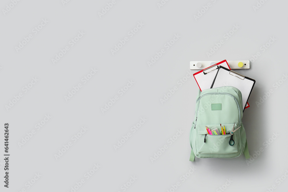 Stylish school backpack with stationery hanging on light wall