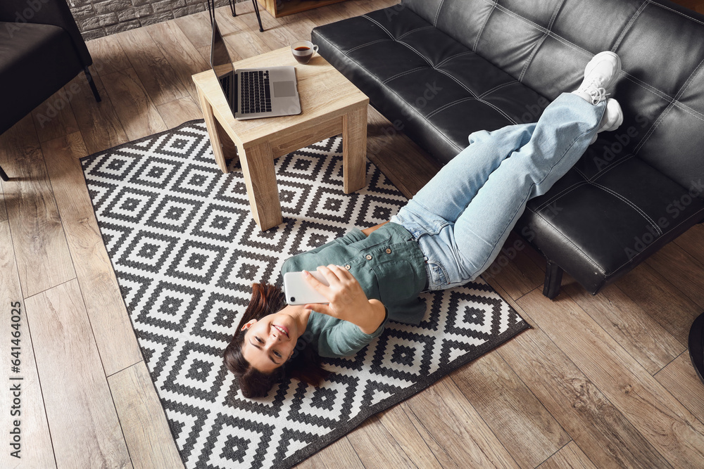 Young woman using mobile phone on carpet in living room