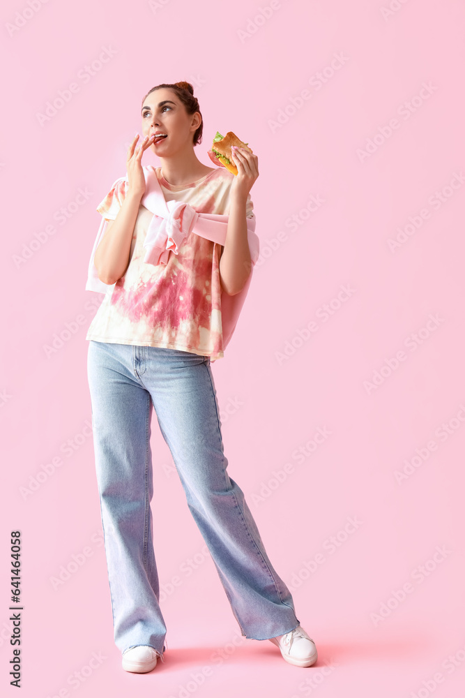 Young woman with tasty sandwich on pink background