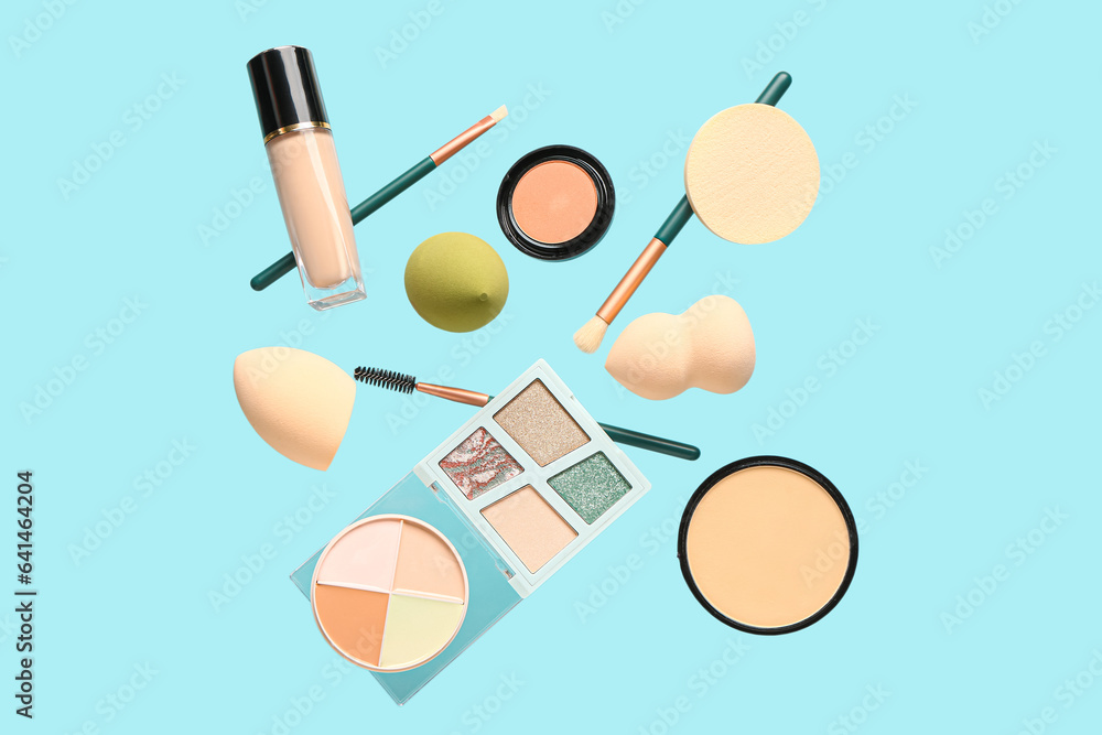 Decorative cosmetics and makeup sponges flying on color background