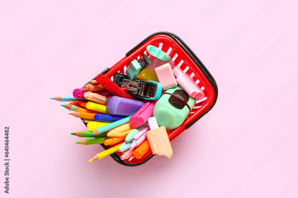 Shopping basket with different stationery on pink background