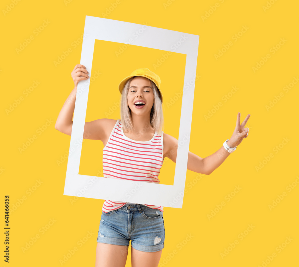 Young beautiful happy woman with frame showing victory gesture on yellow background