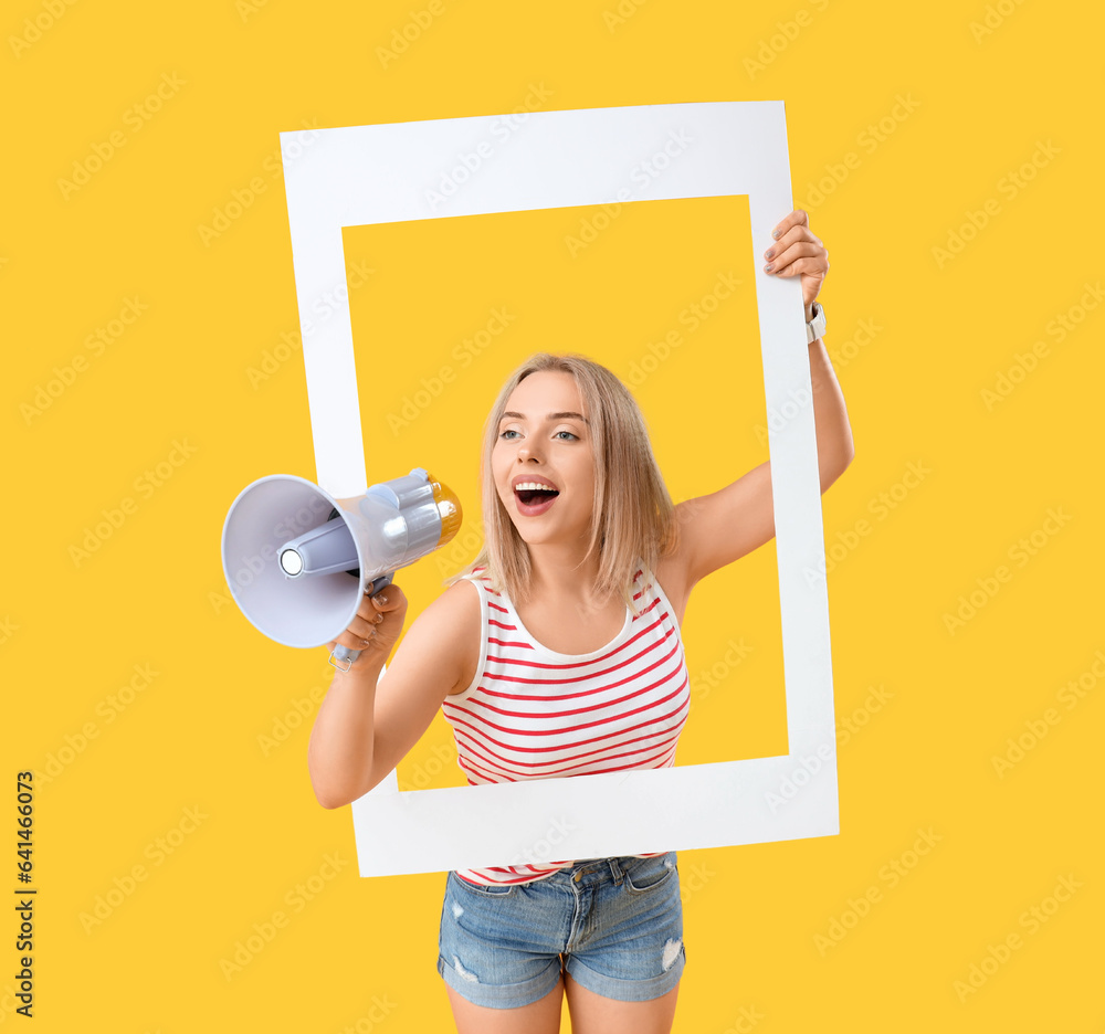 Young beautiful happy woman with frame and megaphone on yellow background