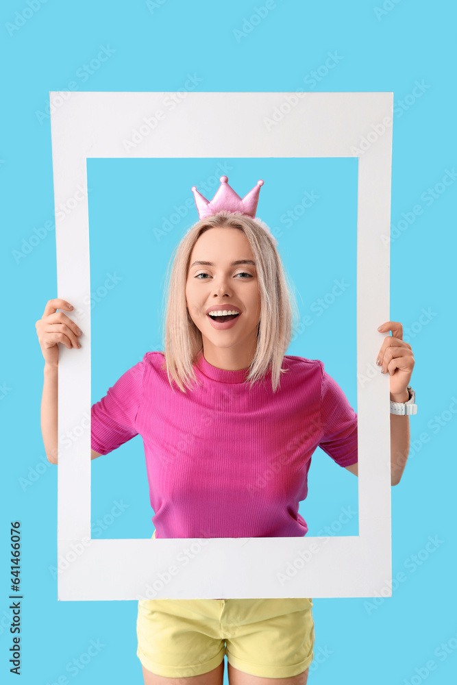 Young beautiful happy woman in party crown with frame on blue background