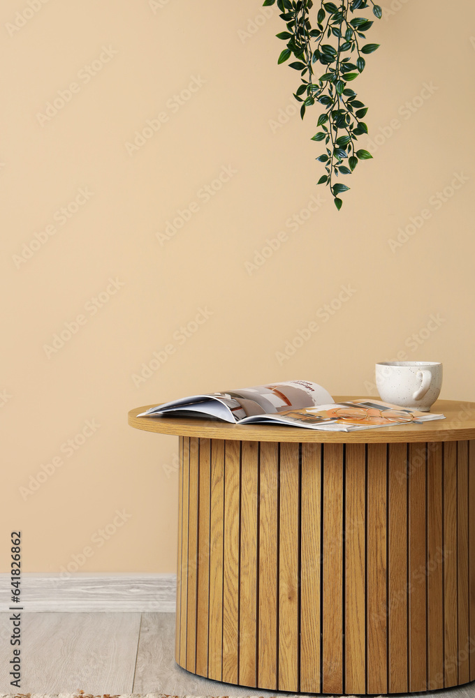 Wooden coffee table with cup and magazine near beige wall