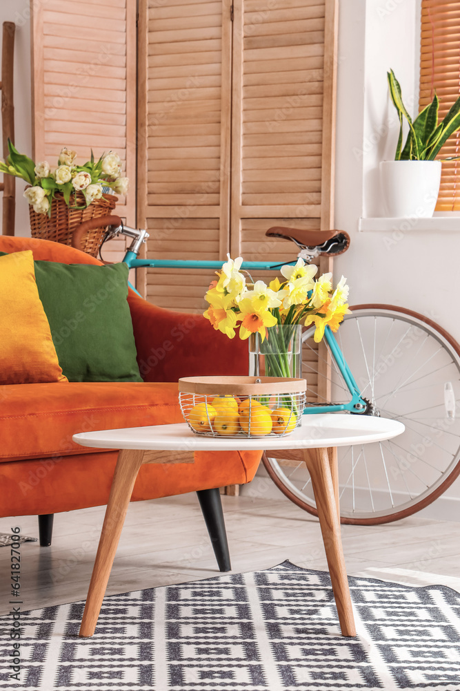 Interior of light living room with cozy brown sofa and narcissus flowers on coffee table