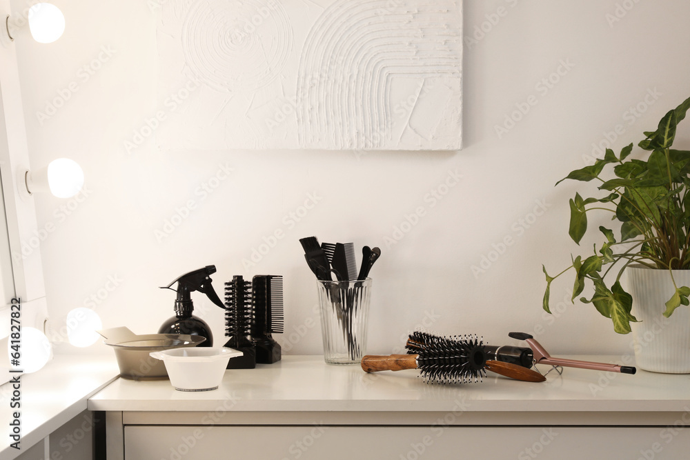 Different hairdressing tools on table near light wall