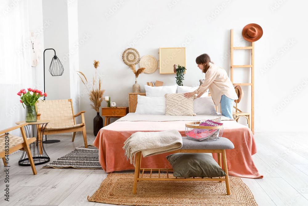 Young woman making bed in light bedroom