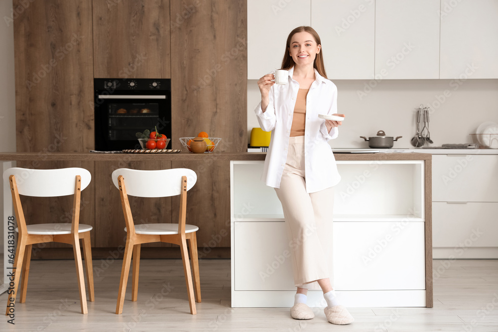 Happy young woman enjoying cup of coffee in modern kitchen