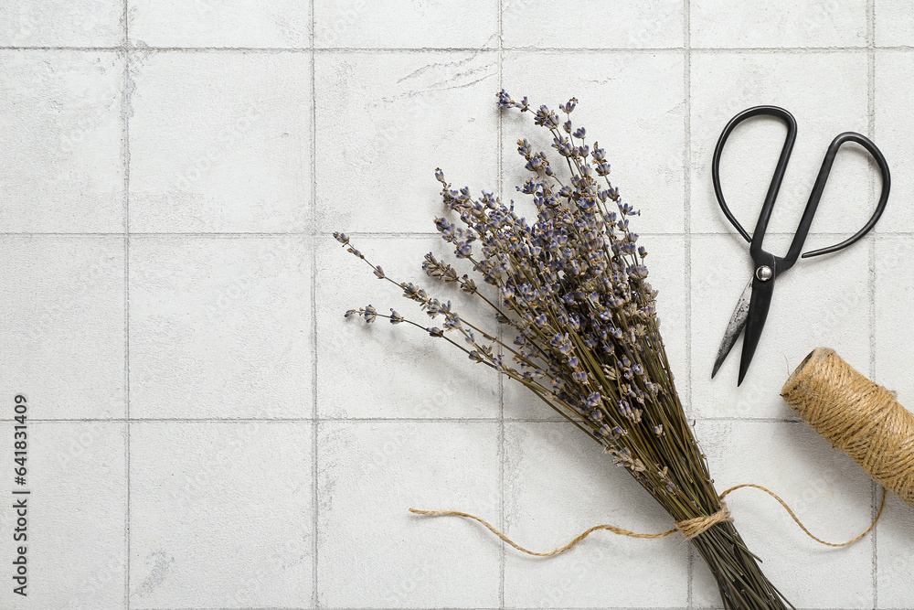 Scissors with thread and dried lavender on white tile background