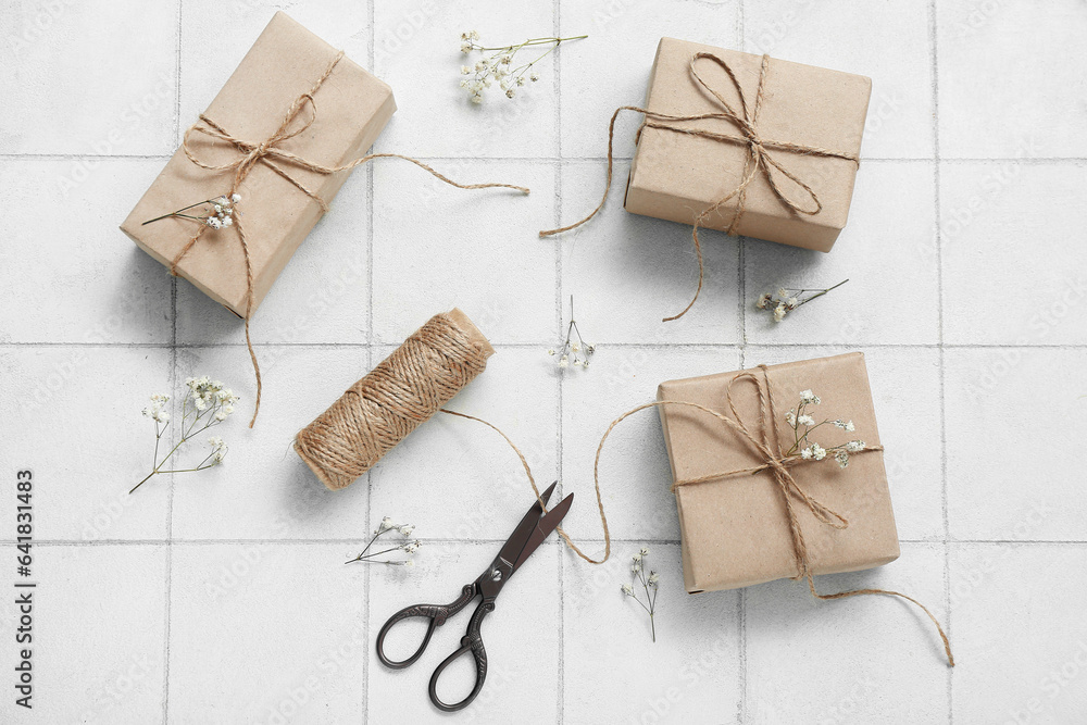 Tied boxes with scissors, thread and dried twigs on white tile background