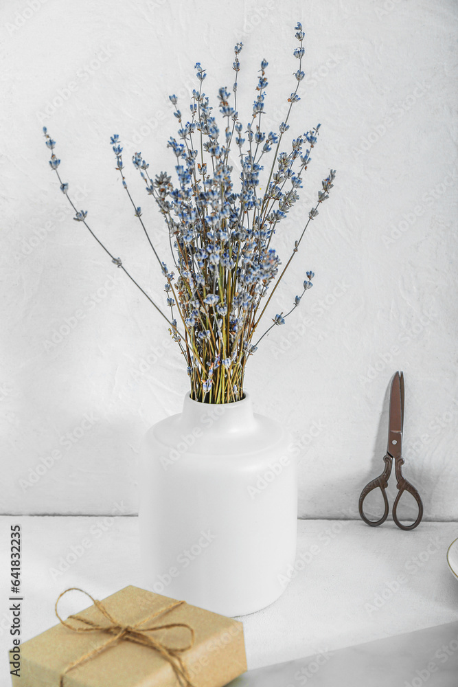 Vase with dried lavender, scissors and tied box on white table near wall