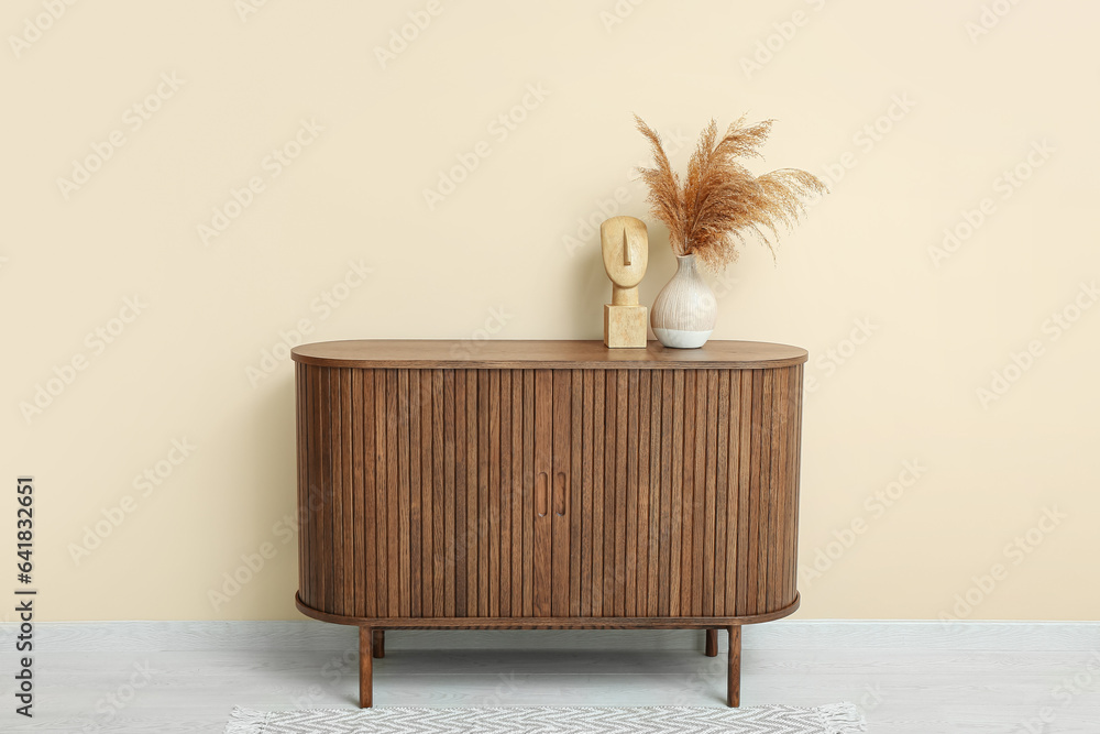 Vase of dried pampas grass with figurine on dresser near beige wall