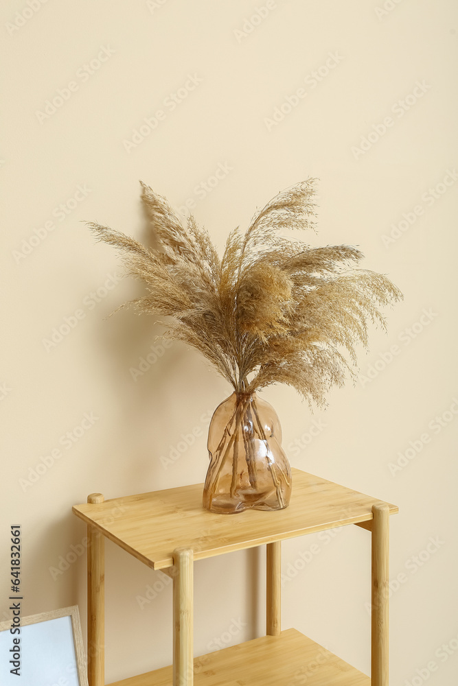 Vase with dried pampas grass on shelving unit near beige wall