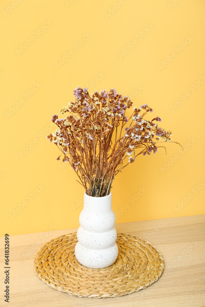 Vase with dried flowers and mat on coffee table near yellow wall