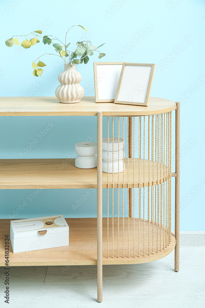 Vase of dried eucalyptus with photo frames on shelving unit near blue wall