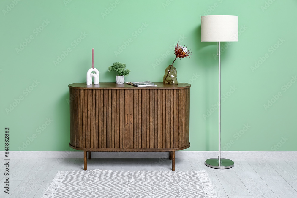 Vase with dried red protea, dresser and floor lamp near green wall