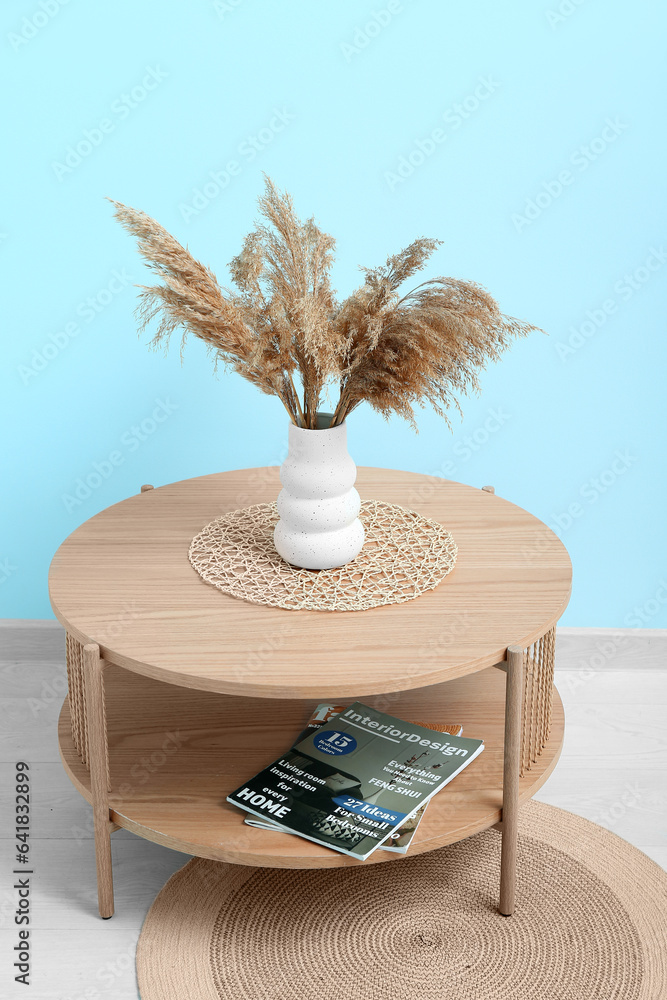 Vase of dried pampas grass with figurine on coffee table near blue wall