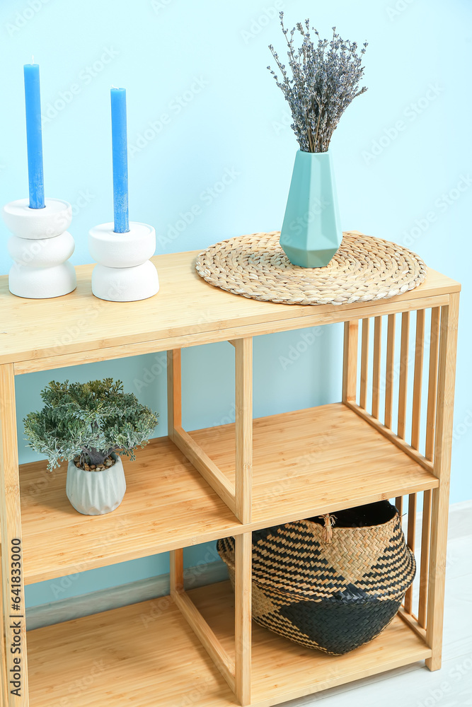 Vase with dried lavender, mat and candles on shelving unit near blue wall