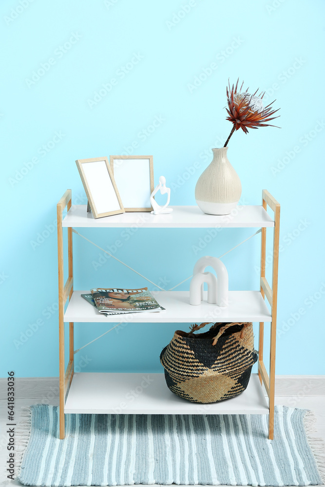 Vase with dried red protea, figurine and photo frames on shelving unit near blue wall