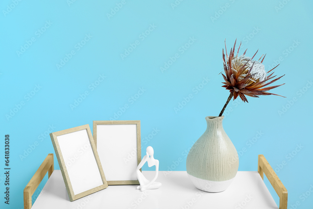 Vase with dried red protea, figurine and photo frames on shelving unit near blue wall