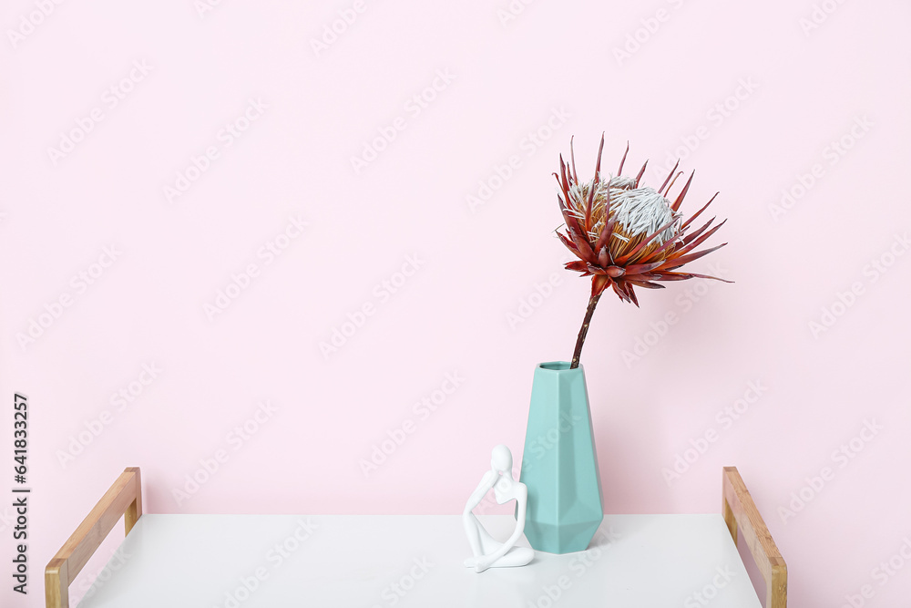 Vase with dried red protea and figurine on shelving unit near pink wall