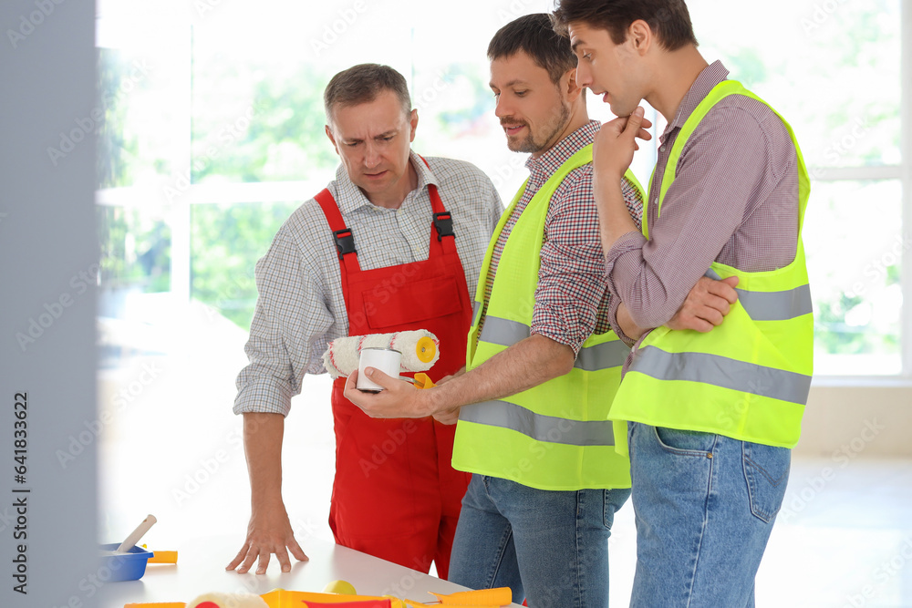 Team of male builders with paint can and roller working in room