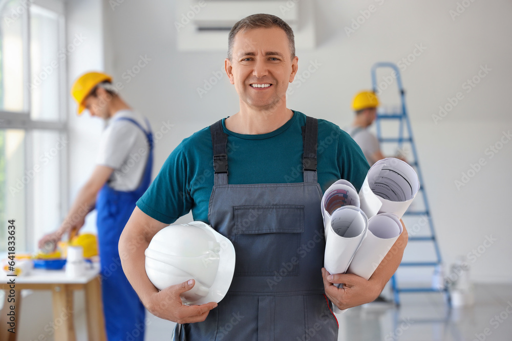 Mature builder with hardhat and paper rolls in room