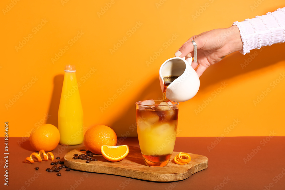 Woman preparing tasty orange espresso on color background