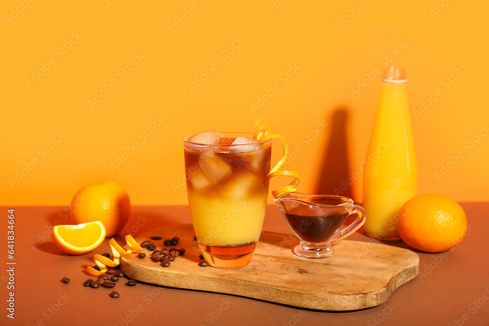 Glass of tasty orange espresso and ingredients on color background