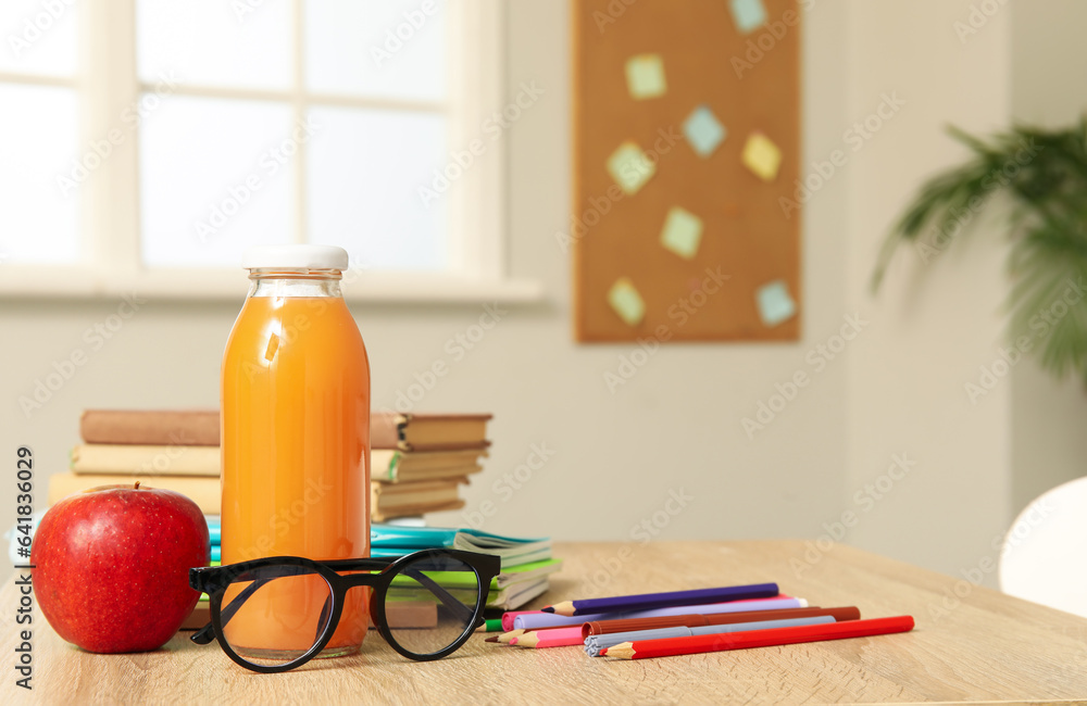 Modern school desk with eyeglasses, lunch and stationery in room near white wall