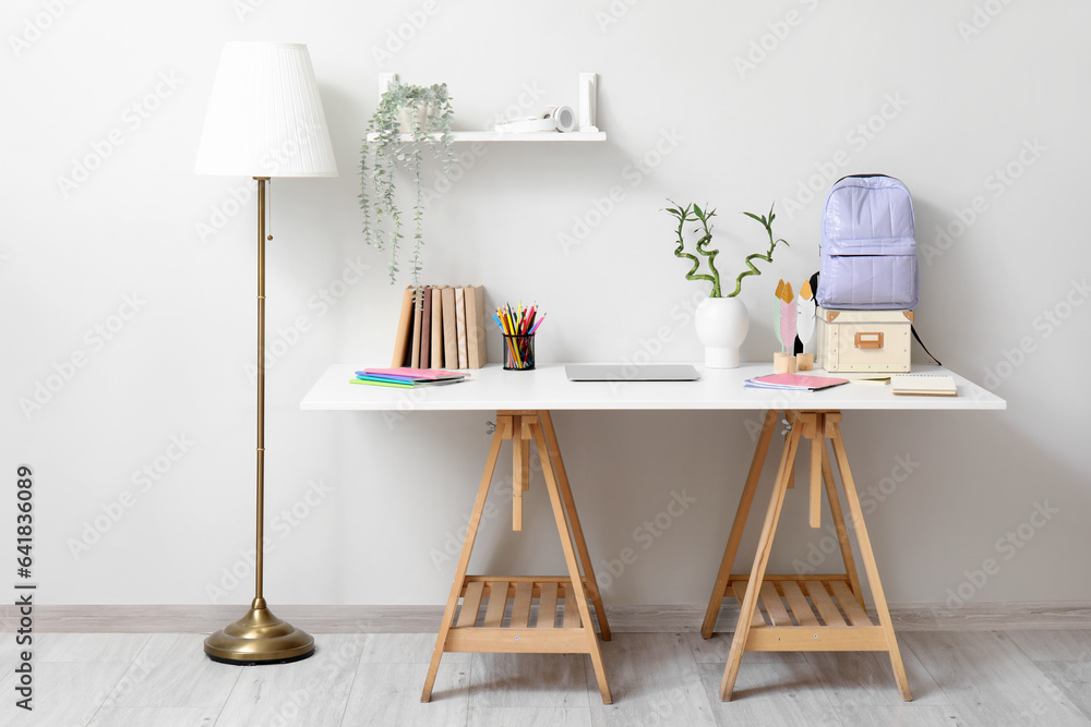 Modern school desk with laptop and stationery in room near white wall