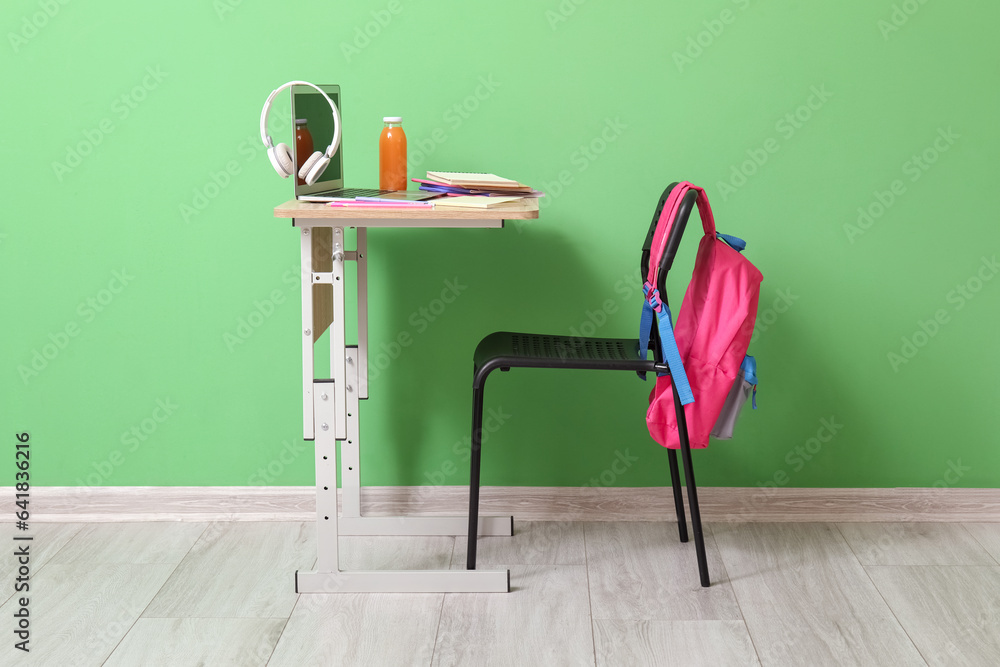 Modern school desk with laptop, gadgets and stationery in room near green wall