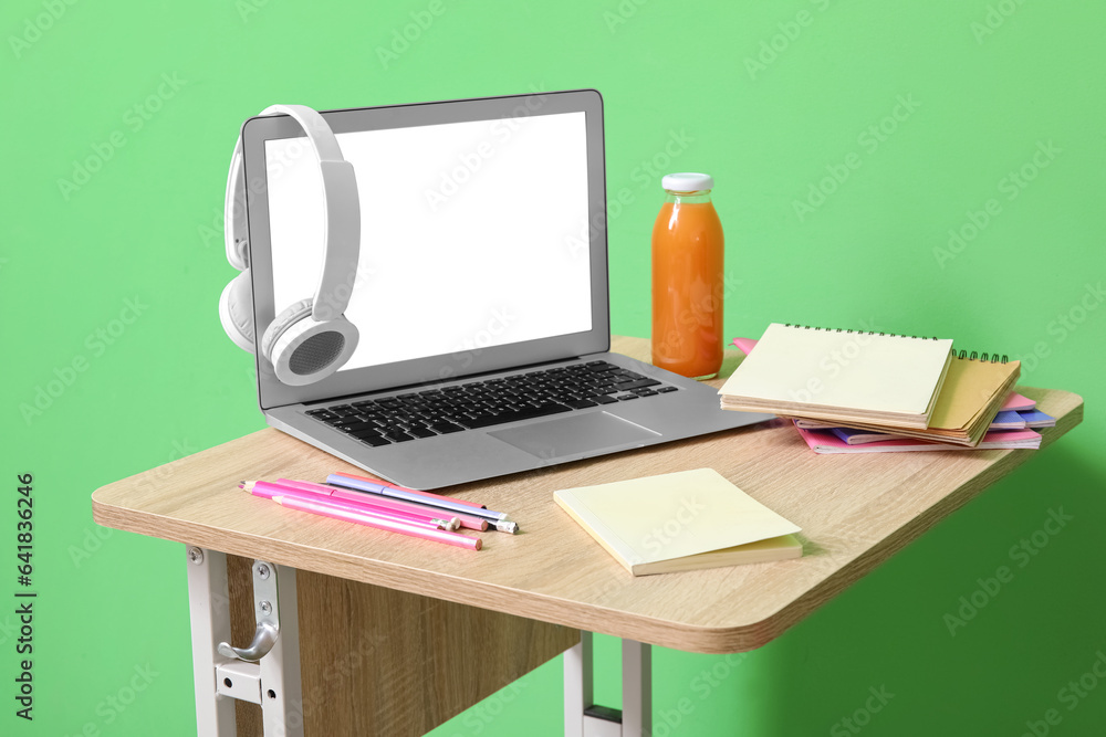 Modern school desk with laptop, gadgets and stationery in room near green wall