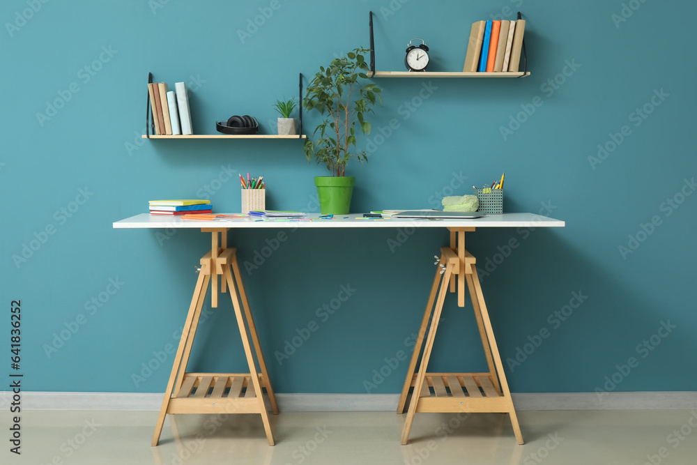 Modern school desk with stationery in room near blue wall