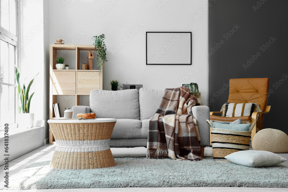 Modern living room interior with grey sofa, coffee table, blanket and wicker basket