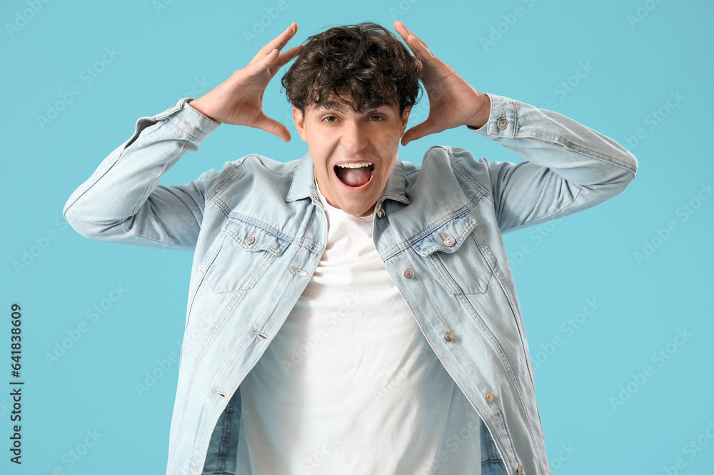 Portrait of angry yelling young man on blue background