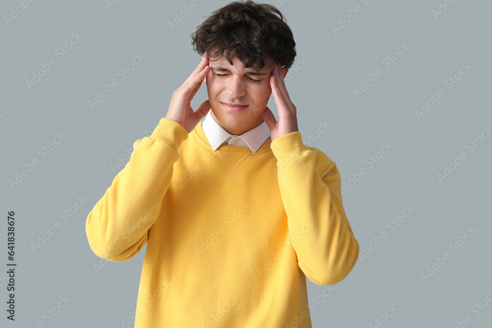 Portrait of young man suffering from headache on grey background