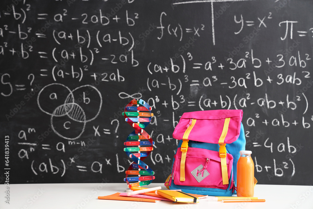 Pink school backpack with stationery, molecular model and bottle of juice on white table near black 