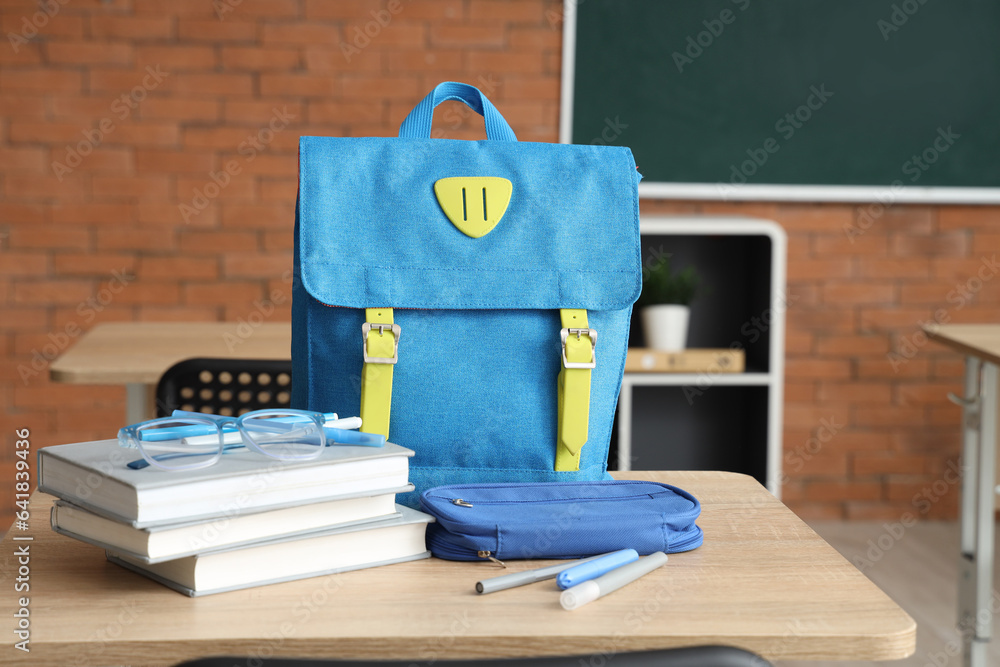 Blue school backpack with stationery and eyeglasses on desk in classroom