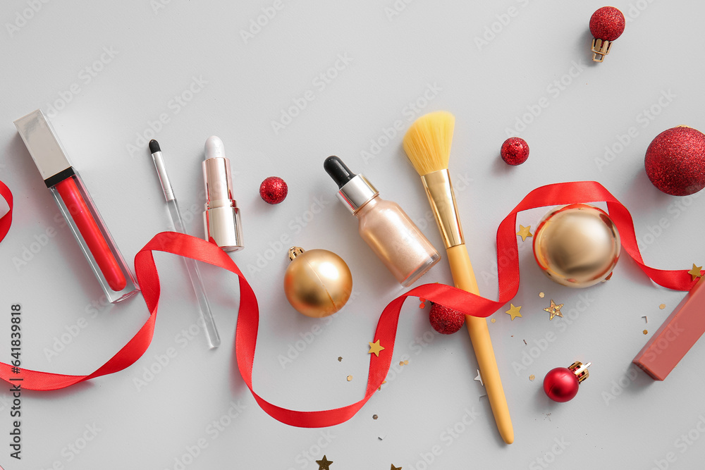 Makeup products and Christmas decorations on grey background