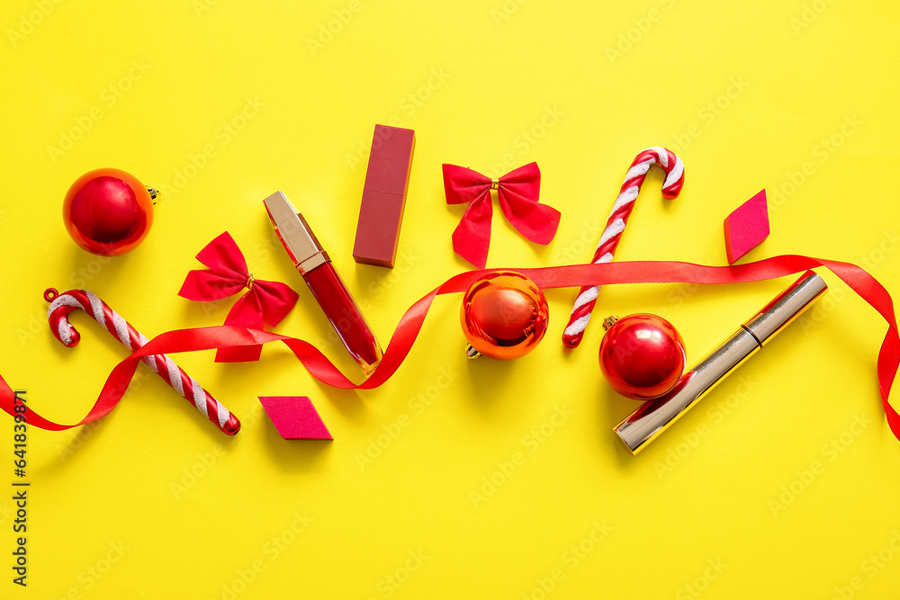 Makeup products and red Christmas decorations on yellow background