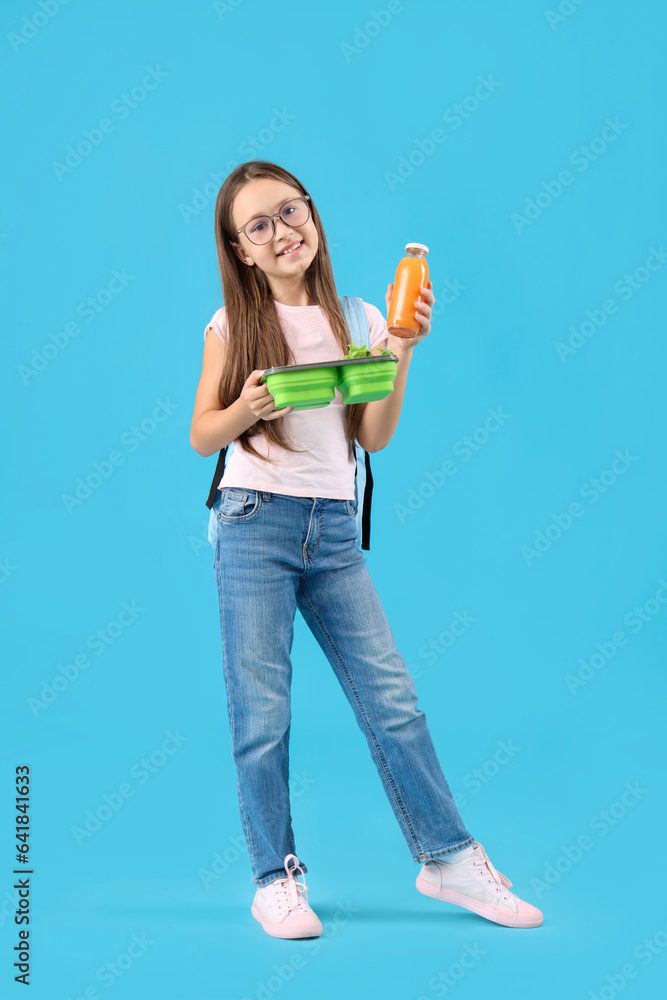 Happy little girl with bottle of juice and lunchbox on blue background