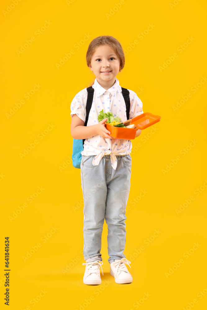 Happy little girl with backpack and lunchbox on yellow background