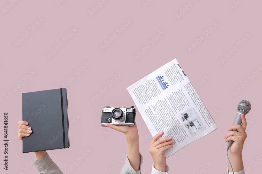 Female hands with newspaper, notebook, microphone and photo camera on color background