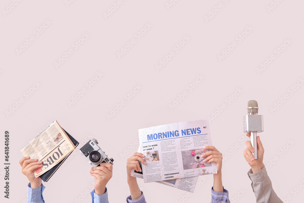 Female hands with newspapers, photo camera and microphone on light background