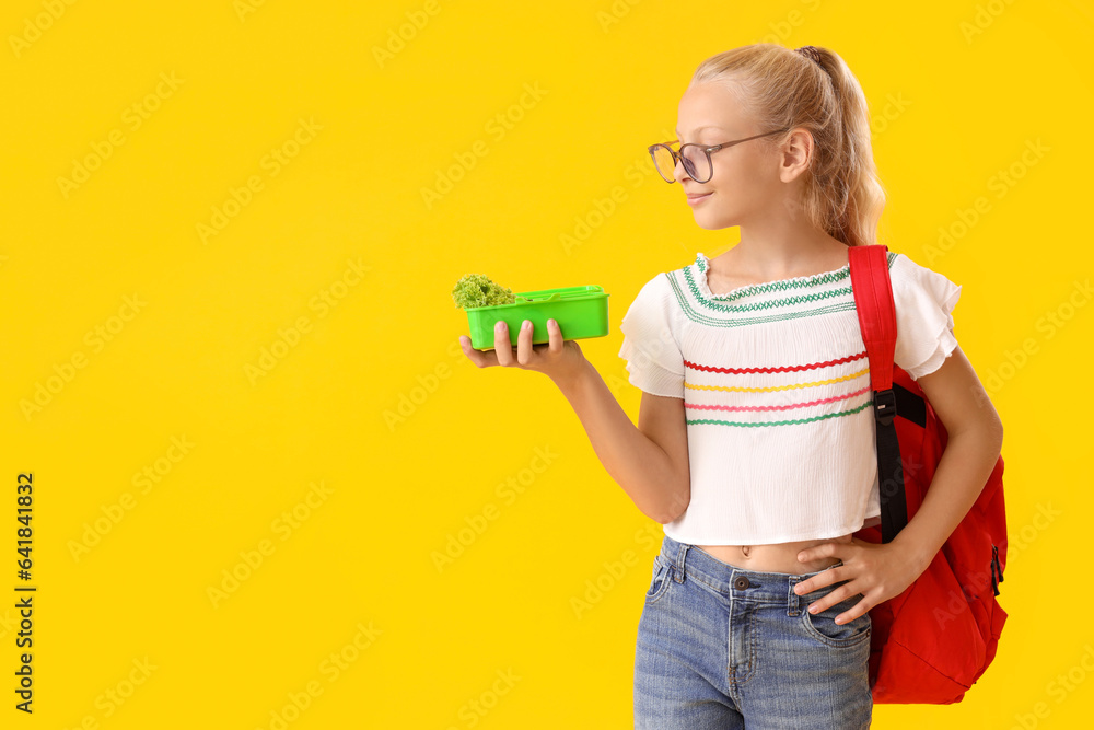 Happy girl in eyeglasses with backpack and lunchbox on yellow background