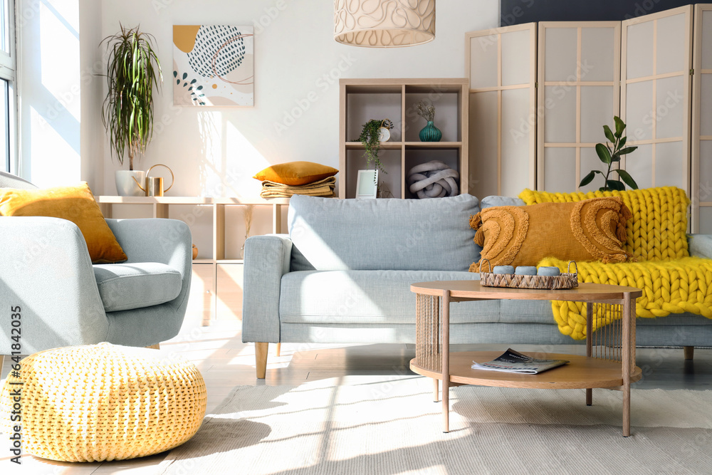 Interior of light living room with  grey sofa, armchair and wooden coffee table