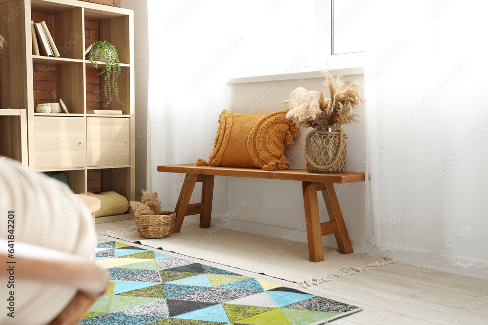 Vase with pampas grass and pillow on wooden bench in living room