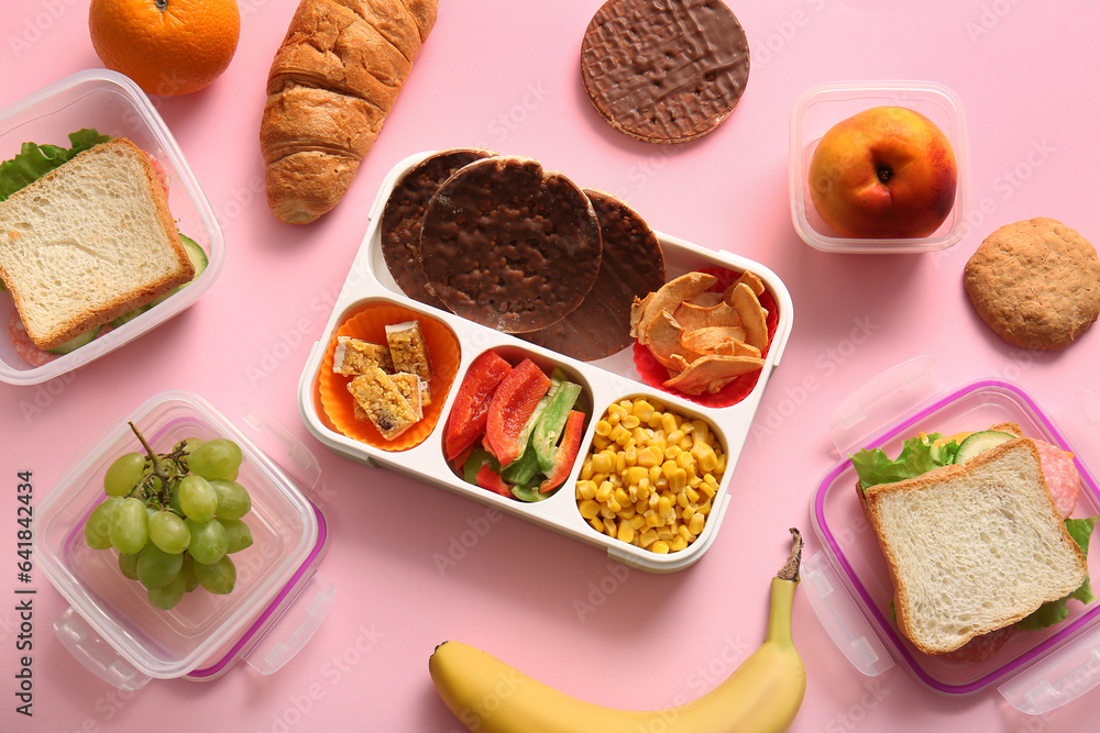 Lunchboxes with different delicious food on pink background